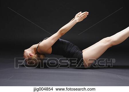 Picture - Attractive young Japanese woman wearing black pants and tank top practicing yoga on black background. Fotosearch