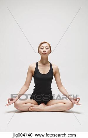 Stock Image - Attractive young Japanese woman wearing black pants and tank top practicing yoga on white background. Fotosearch
