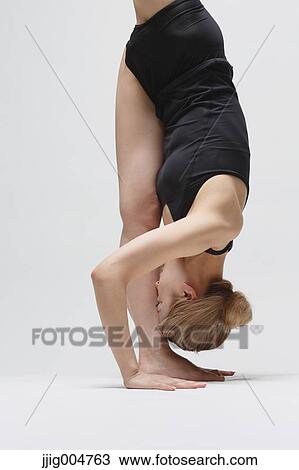 Stock Image - Attractive young Japanese woman wearing black pants and tank top practicing yoga on white background. Fotosearch