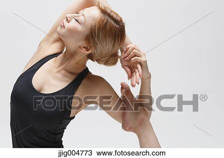 Stock Image - Attractive young Japanese woman wearing black pants and tank top practicing yoga on white background. Fotosearch
