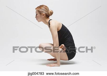Stock Image - Attractive young Japanese woman wearing black pants and tank top practicing yoga on white background. Fotosearch