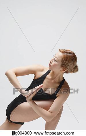 Stock Image - Attractive young Japanese woman wearing black pants and tank top practicing yoga on white background. Fotosearch