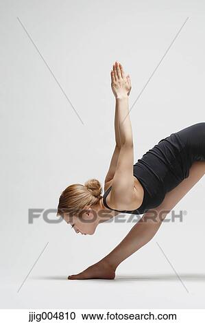 Stock Image - Attractive young Japanese woman wearing black pants and tank top practicing yoga on white background. Fotosearch