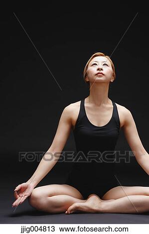 Stock Image - Attractive young Japanese woman wearing black pants and tank top practicing yoga on black background. Fotosearch