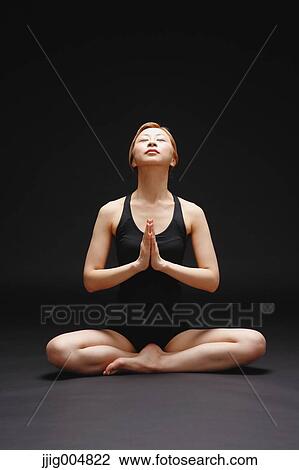 Stock Image - Attractive young Japanese woman wearing black pants and tank top practicing yoga on black background. Fotosearch