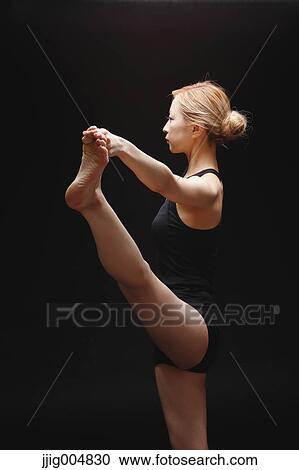 Stock Image - Attractive young Japanese woman wearing black pants and tank top practicing yoga on black background. Fotosearch