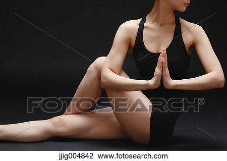Stock Image - Attractive young Japanese woman wearing black pants and tank top practicing yoga on black background. Fotosearch