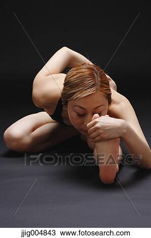 Stock Image - Attractive young Japanese woman wearing black pants and tank top practicing yoga on black background. Fotosearch