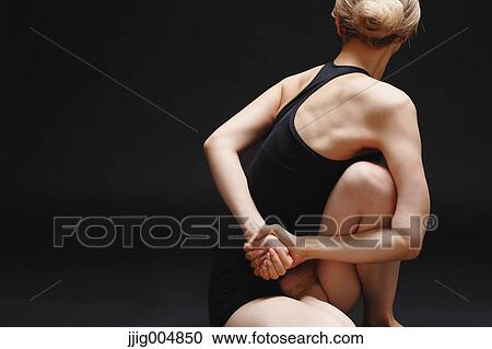 Stock Image - Attractive young Japanese woman wearing black pants and tank top practicing yoga on black background. Fotosearch