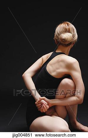 Stock Image - Attractive young Japanese woman wearing black pants and tank top practicing yoga on black background. Fotosearch