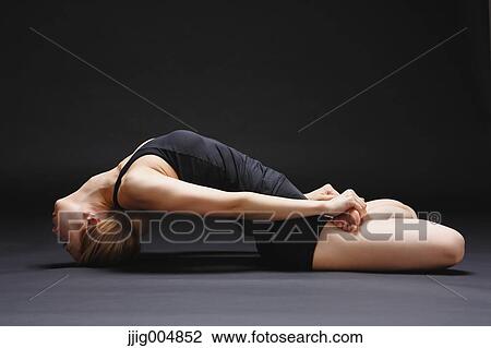 Stock Image - Attractive young Japanese woman wearing black pants and tank top practicing yoga on black background. Fotosearch