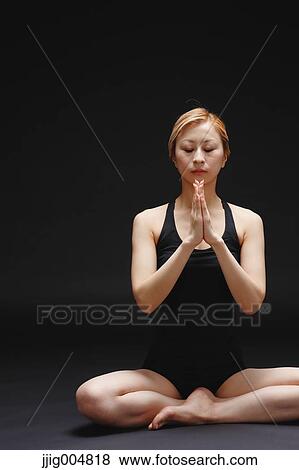 Stock Photo - Attractive young Japanese woman wearing black pants and tank top practicing yoga on black background. Fotosearch