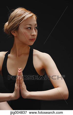 Stock Photo - Attractive young Japanese woman wearing black pants and tank top practicing yoga on black background. Fotosearch