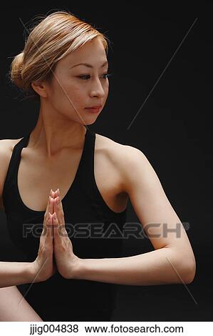 Stock Photo - Attractive young Japanese woman wearing black pants and tank top practicing yoga on black background. Fotosearch