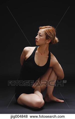 Stock Photo - Attractive young Japanese woman wearing black pants and tank top practicing yoga on black background. Fotosearch