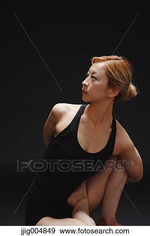 Stock Photo - Attractive young Japanese woman wearing black pants and tank top practicing yoga on black background. Fotosearch
