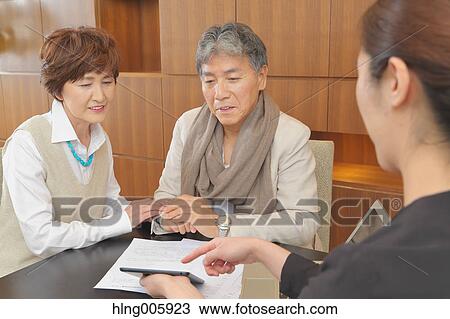 Stock Image - Fashionable Japanese senior couple discussing with advisor. Fotosearch