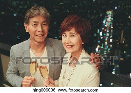 Stock Photograph - Fashionable Japanese senior couple toasting in front of night cityscape. Fotosearch