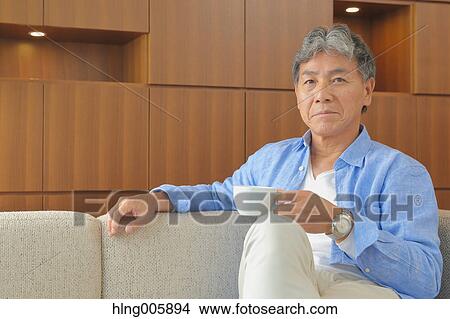 Fashionable Japanese senior man having a cup of coffee on the sofa View Large Photo Image Picture - Fashionable Japanese senior man having a cup of coffee on the sofa. Fotosearch