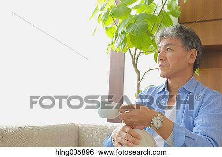 Stock Photograph - Fashionable Japanese senior man having a cup of coffee on the sofa. Fotosearch