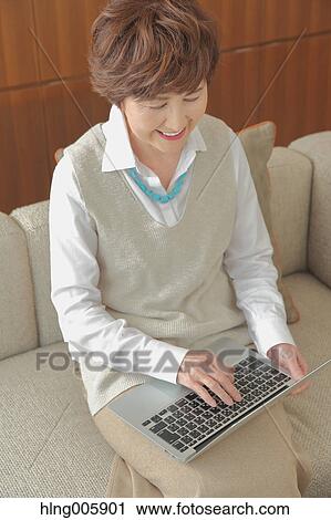 Stock Image - Fashionable Japanese senior woman working with laptop. Fotosearch