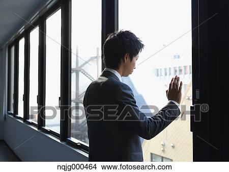 Japanese businessman looking out of the window in empty office View Large Photo Image Picture - Japanese businessman looking out of the window in empty office. Fotosearch
