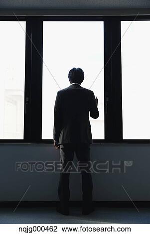 Stock Image - Japanese businessman looking out of the window in empty office. Fotosearch