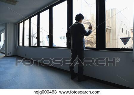 Stock Image - Japanese businessman looking out of the window in empty office. Fotosearch
