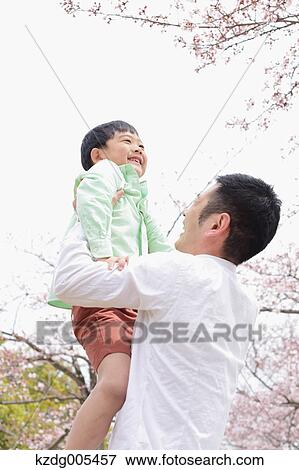 Stock Photo - Japanese father and son with cherry blossoms in a city park. Fotosearch