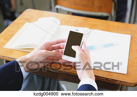Stock Image - Japanese high-school student using smartphone during a lesson. Fotosearch