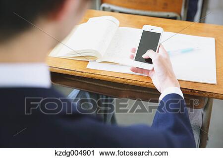Stock Image - Japanese high-school student using smartphone during a lesson. Fotosearch