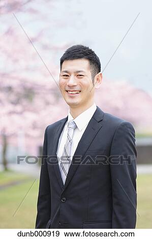 Stock Photo - Japanese man with cherry blossoms in a city park. Fotosearch