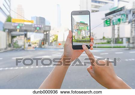 Stock Photograph - Japanese woman using augumented reality app on smartphone downtown Tokyo, Japan. Fotosearch