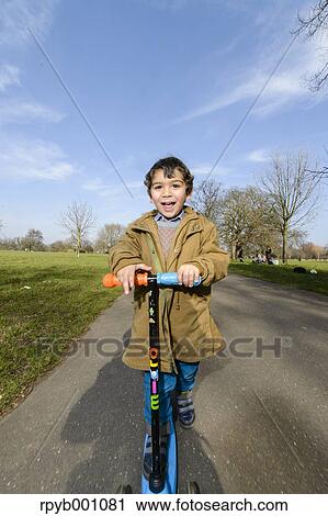 Kid playing with kickboard in a park View Large Photo Image Stock Image - Kid playing with kickboard in a park. Fotosearch