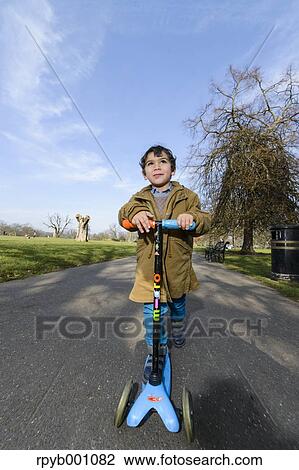 Kid playing with kickboard in a park View Large Photo Image Stock Image - Kid playing with kickboard in a park. Fotosearch