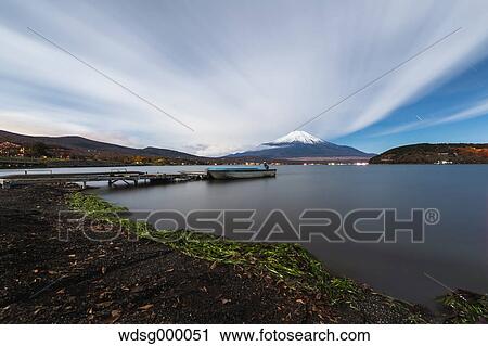 Stock Image - Night view of cloudy sky and Mount Fuji at night from Lake Yamanaka, Yamanashi Prefecture, Japan. Fotosearch