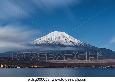 Stock Image - Night view of cloudy sky and Mount Fuji at night from Lake Yamanaka, Yamanashi Prefecture, Japan. Fotosearch