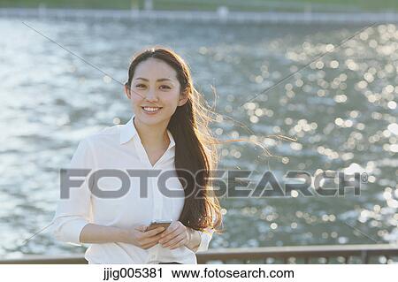 Stock Image - Portrait of young Japanese businesswoman by a river downtown Tokyo. Fotosearch