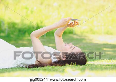 Portrait of young Japanese woman laying on grass with smartphone View Large Photo Image Picture - Portrait of young Japanese woman laying on grass with smartphone. Fotosearch