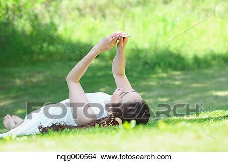 Portrait of young Japanese woman laying on grass with smartphone View Large Photo Image Picture - Portrait of young Japanese woman laying on grass with smartphone. Fotosearch