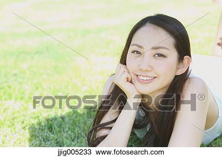 Stock Image - Portrait of young Japanese woman laying on green grass. Fotosearch