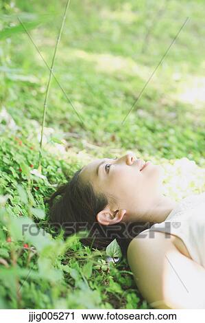 Stock Image - Portrait of young Japanese woman laying on green grass. Fotosearch