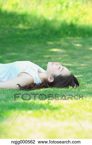 Stock Image - Portrait of young Japanese woman laying on green grass. Fotosearch