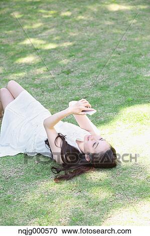 Portrait of young Japanese woman laying on grass with smartphone View Large Photo Image Stock Image - Portrait of young Japanese woman laying on grass with smartphone. Fotosearch