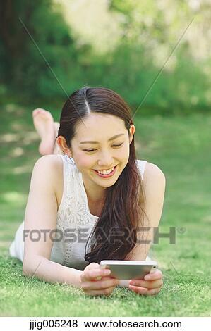 Portrait of young Japanese woman laying on grass with smartphone View Large Photo Image Stock Photo - Portrait of young Japanese woman laying on grass with smartphone. Fotosearch