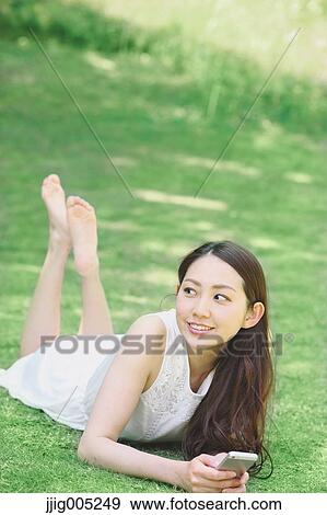 Portrait of young Japanese woman laying on grass with smartphone View Large Photo Image Stock Photo - Portrait of young Japanese woman laying on grass with smartphone. Fotosearch