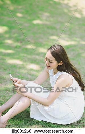 Portrait of young Japanese woman laying on grass with smartphone View Large Photo Image Stock Photo - Portrait of young Japanese woman laying on grass with smartphone. Fotosearch