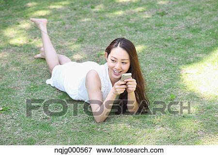Portrait of young Japanese woman laying on grass with smartphone View Large Photo Image Stock Photo - Portrait of young Japanese woman laying on grass with smartphone. Fotosearch