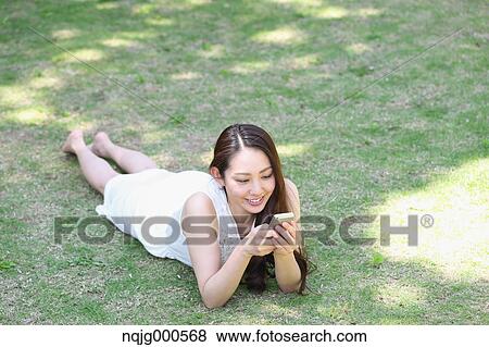 Portrait of young Japanese woman laying on grass with smartphone View Large Photo Image Stock Photo - Portrait of young Japanese woman laying on grass with smartphone. Fotosearch