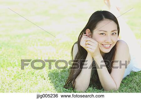 Stock Photograph - Portrait of young Japanese woman laying on green grass. Fotosearch